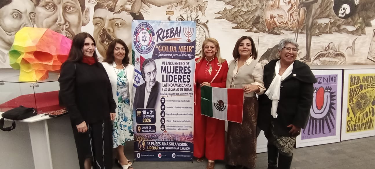 Mujeres participantes del VI Encuentro Golda Meir junto al cartel del evento y la bandera de México.